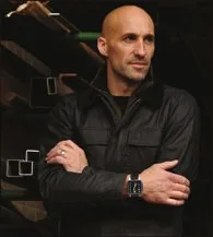 The watchmaker poses confidently in his workshop, wearing one of his signature timepieces on his wrist.