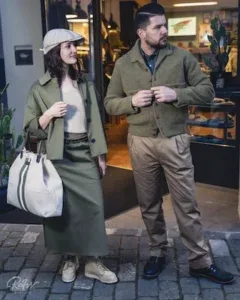 A well-dressed couple in earth-tone heritage outfits stroll past a boutique storefront.