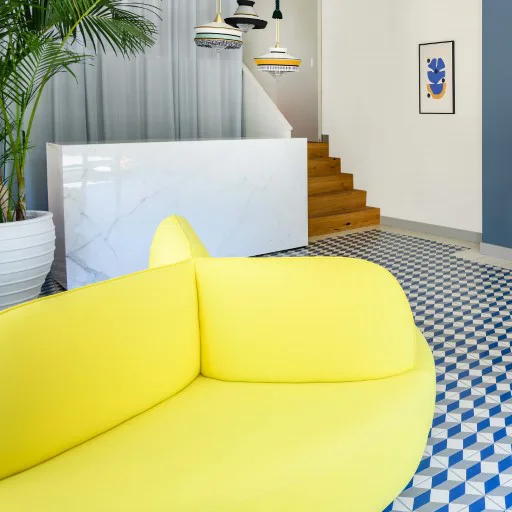 Close-up of the vibrant yellow curved sofa and geometric patterned floor inside the salon.