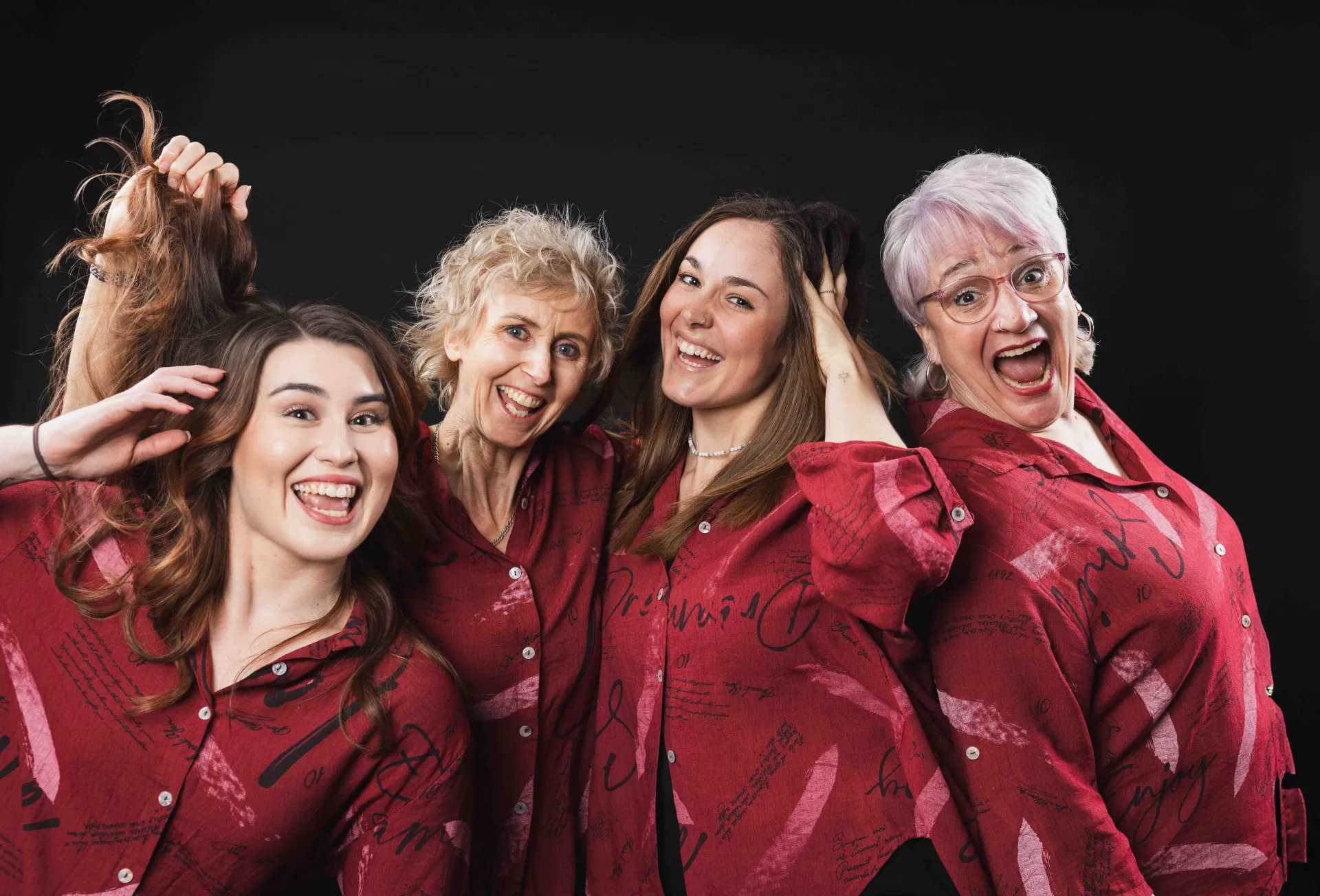 Four women in matching red patterned shirts pose together smiling warmly in a professional studio setting.