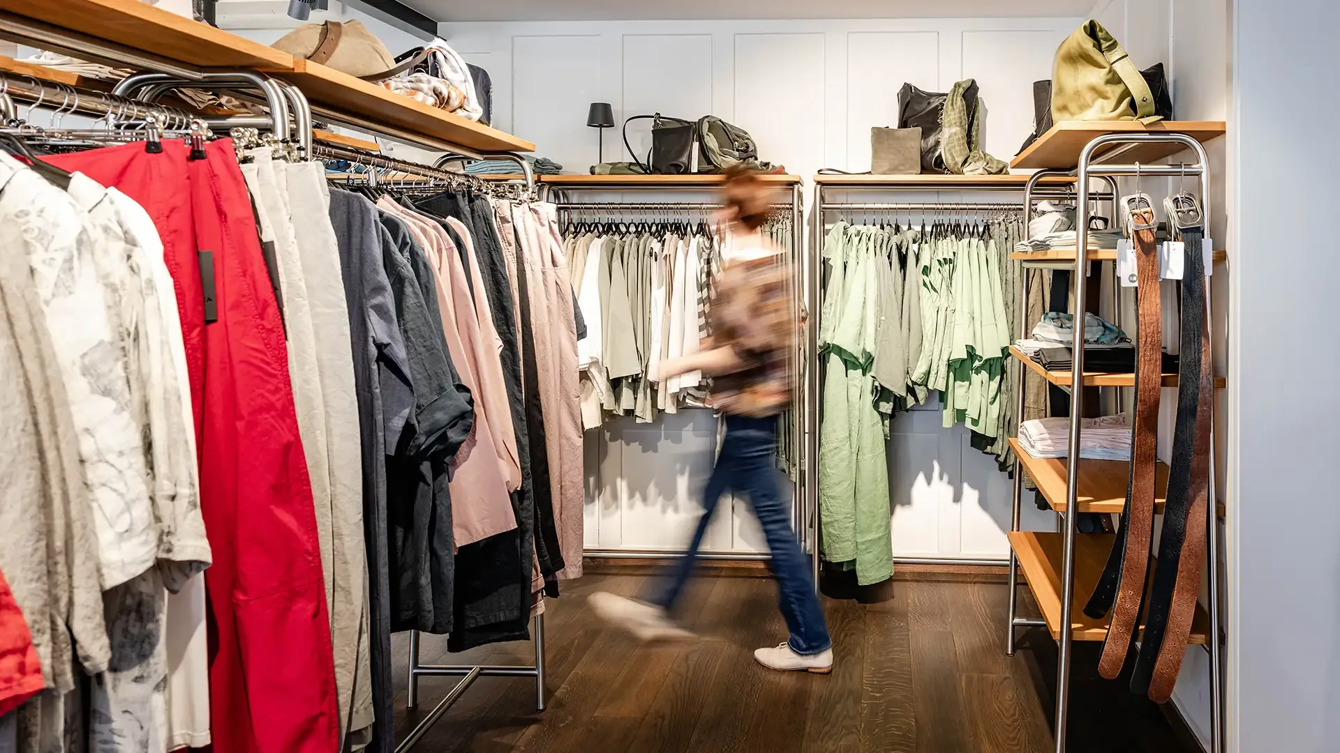 A staff member moves briskly through a well-organized back room filled with neutral and green clothing rails.