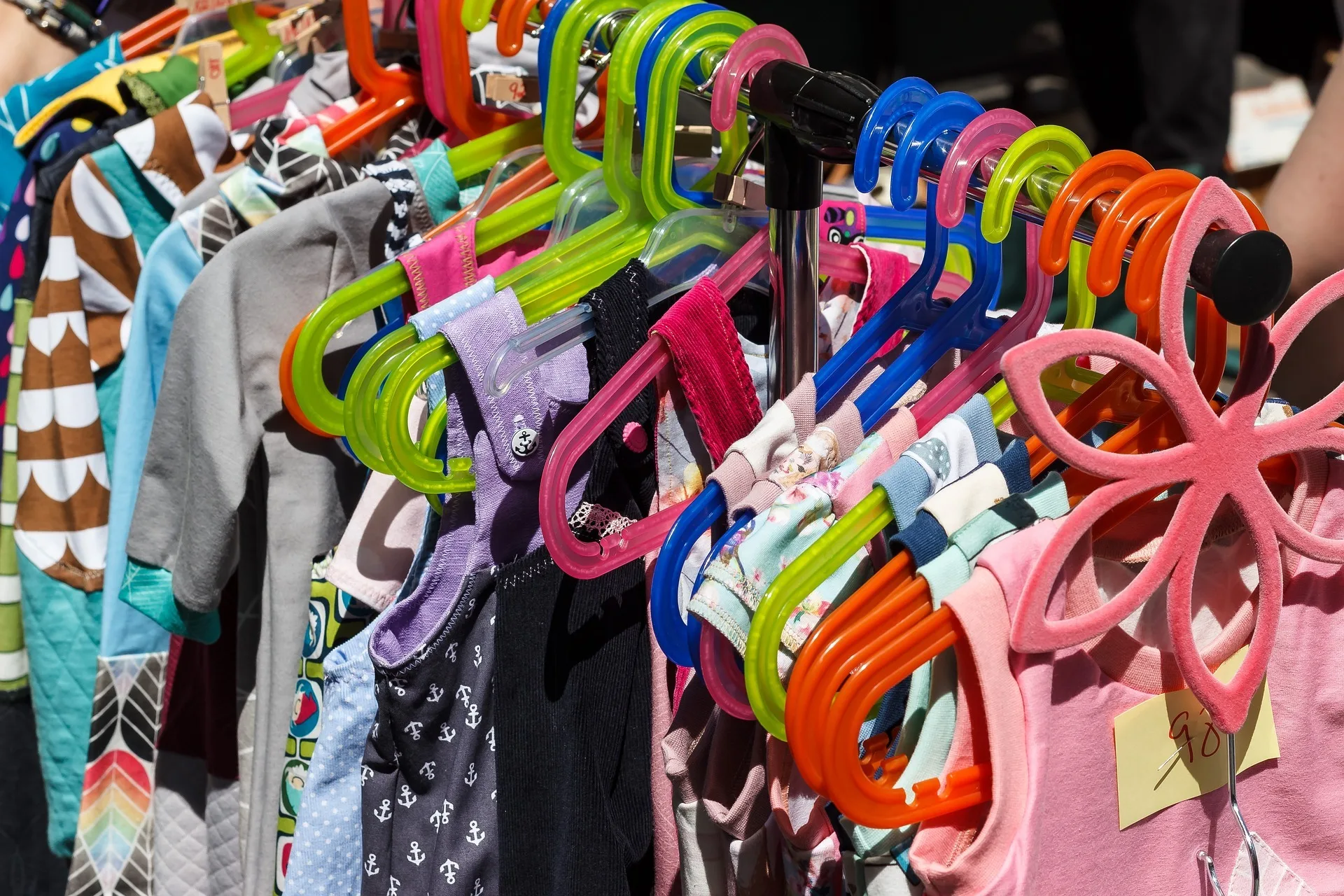 A busy rack of colorful clothes on multicolored hangers at a family second-hand shop.