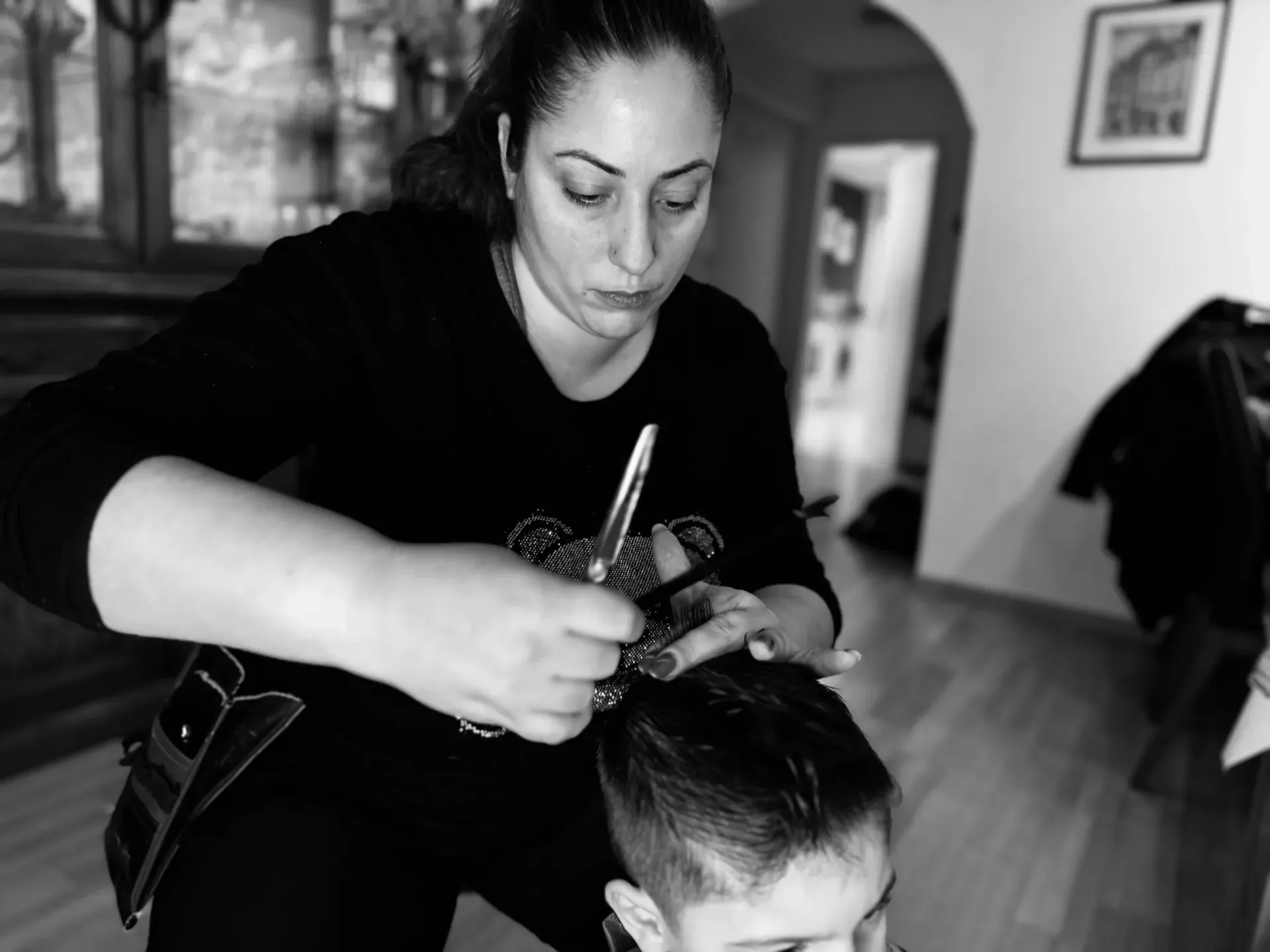 Black-and-white action shot of a female stylist carefully cutting a boy's hair, capturing the skilled craftsmanship central to the salon's identity.
