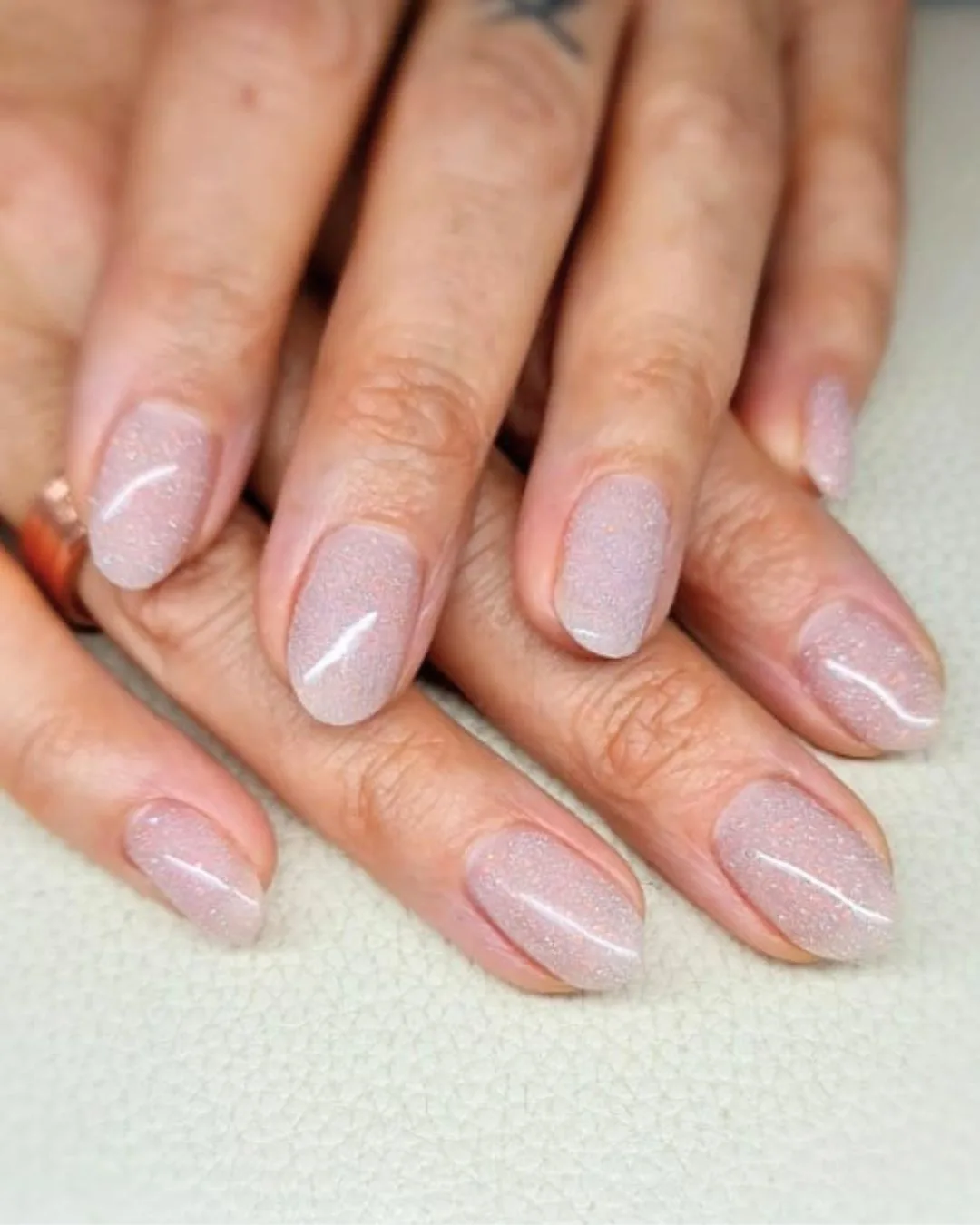 Elegant short round nails with subtle iridescent glitter polish — embodies the refined, understated nail care this Baar studio specializes in.