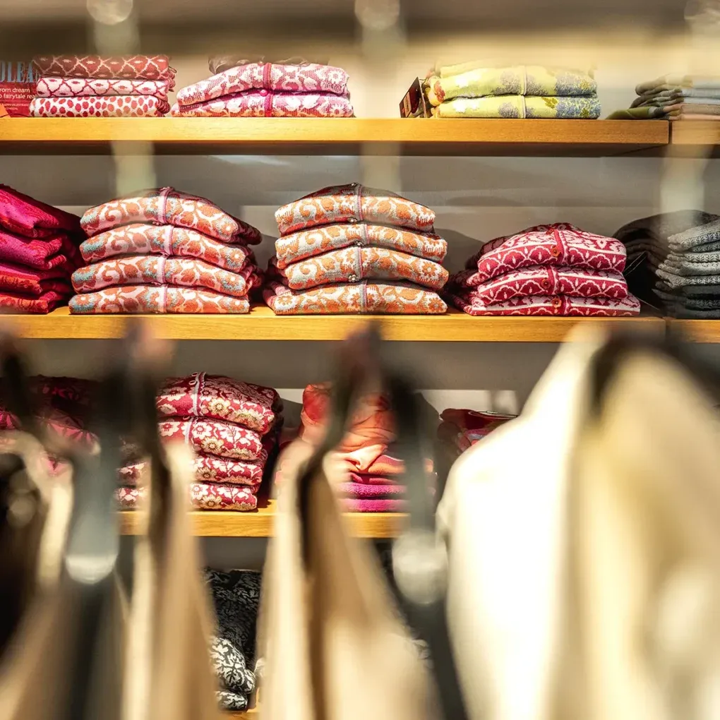 Wooden shelves display neatly folded colorful patterned knitwear cardigans in rich reds, oranges, and pinks.