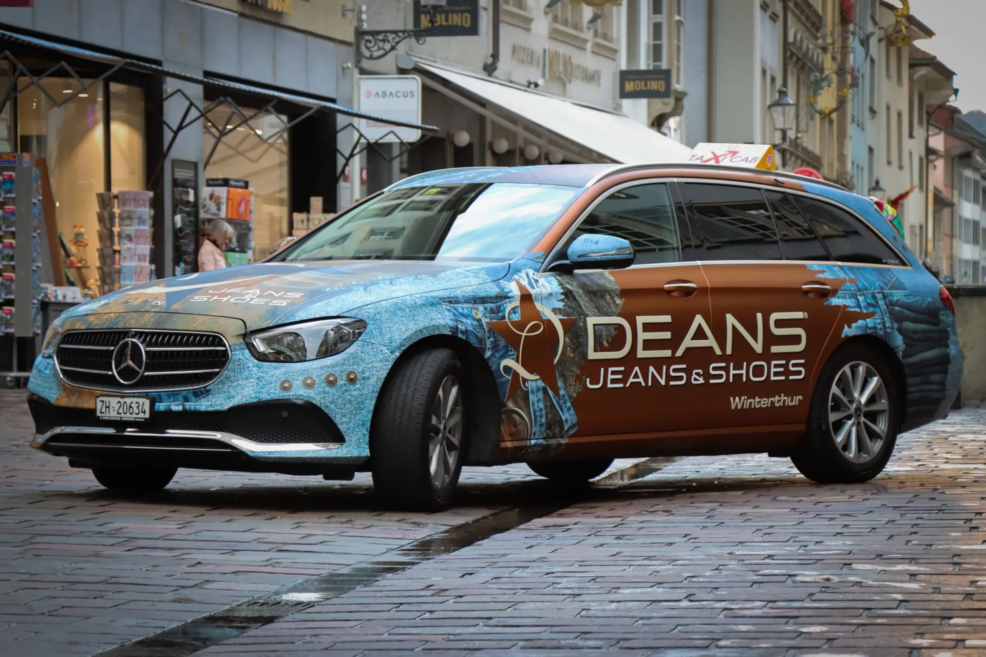 Branded Deans Jeans & Shoes Mercedes estate taxi parked on a cobbled street in Winterthur.