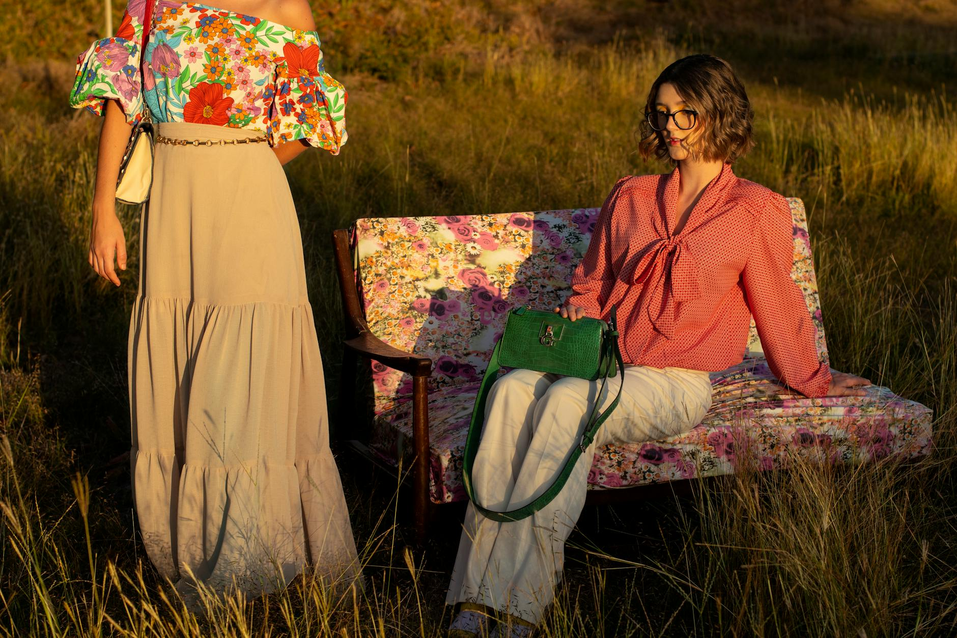 Eine Frau trägt eine bunte Boho-Bluse mit Blumenmuster und High-Waist-Jeans im Retro-Stil der 70er, lässig in einer Frühlingsumgebung posierend.