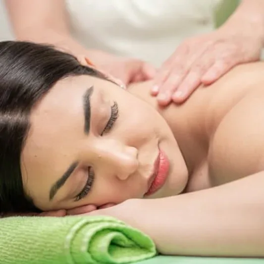 Olivera Mandic in her studio uniform performing a facial massage on a client lying on a treatment table, conveying professional warmth and skilled touch.