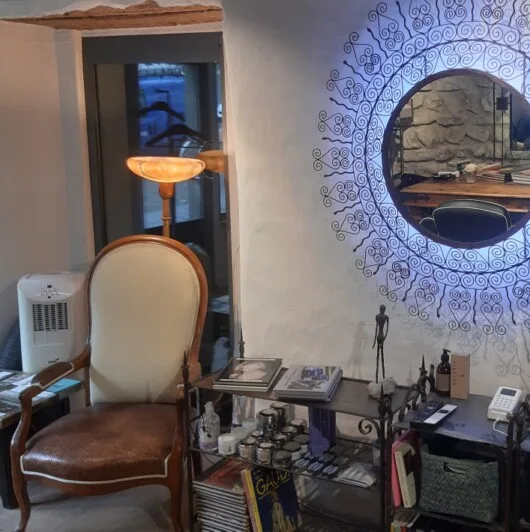 The salon interior shows a vintage armchair beside a glowing decorative round mirror.
