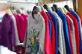 Colorful children's jackets hang densely on a clothing rack in a well-stocked kids' store.